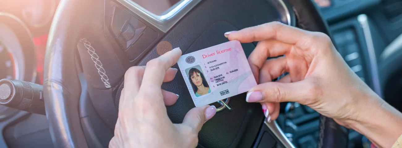 persona sostiene su licencia de conducir sobre el volante de su auto